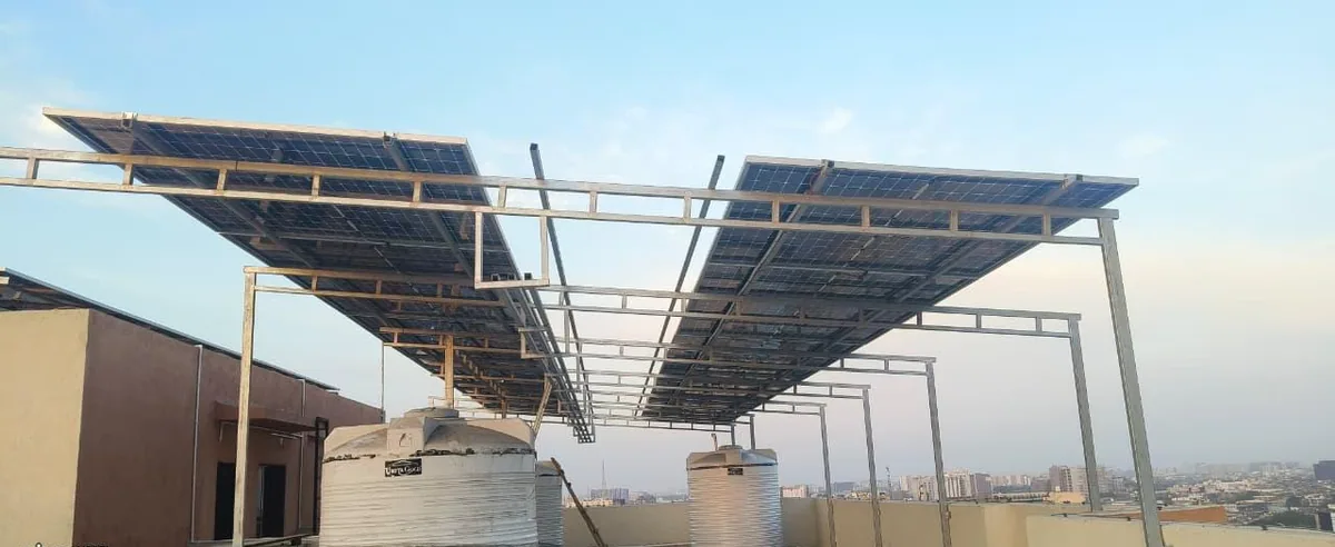 Underside view of two elevated solar arrays with a central service corridor and rooftop water tanks